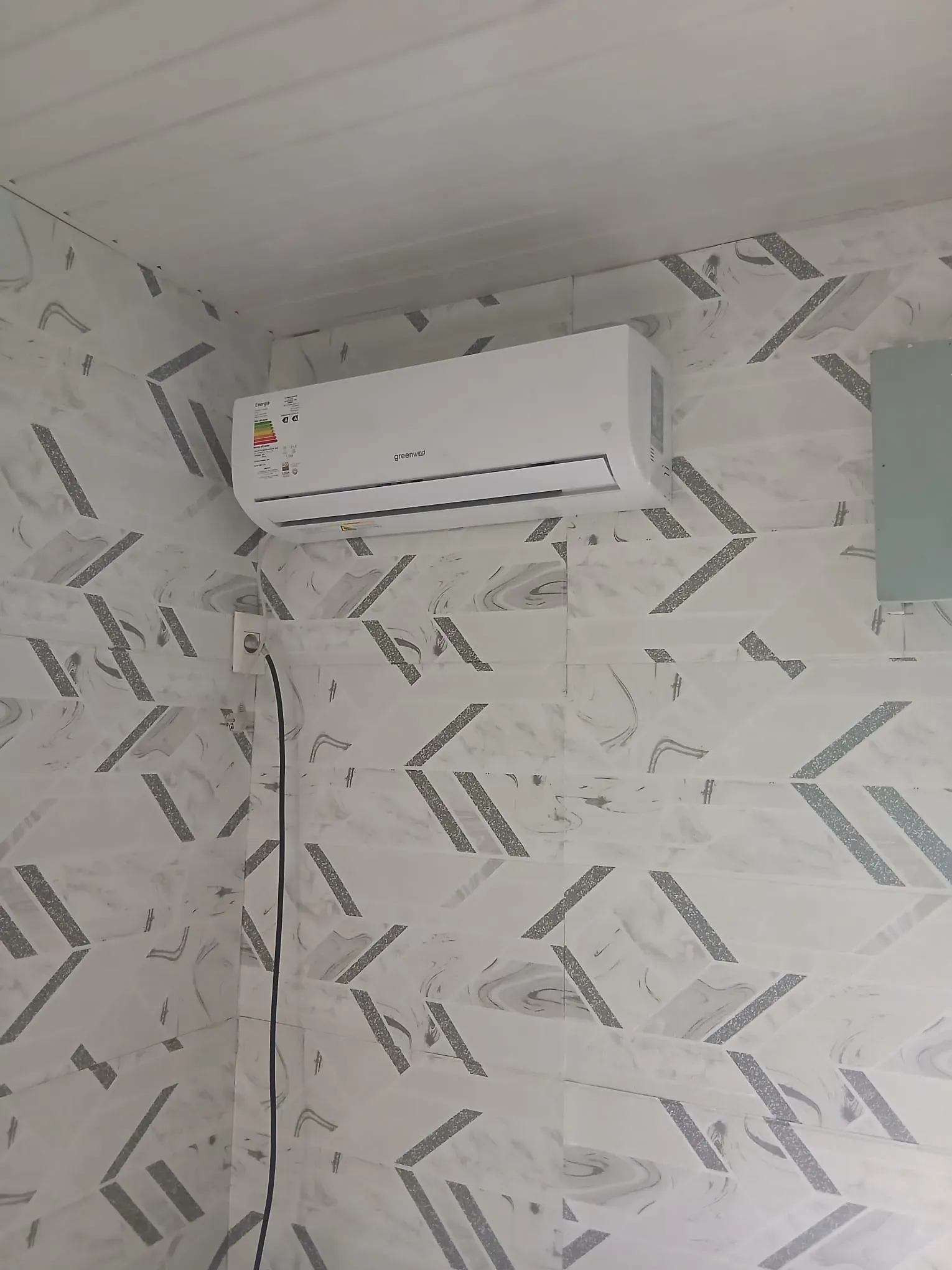 Aire acondicionado split Greenwind instalado en una pared con azulejos, cerca del techo